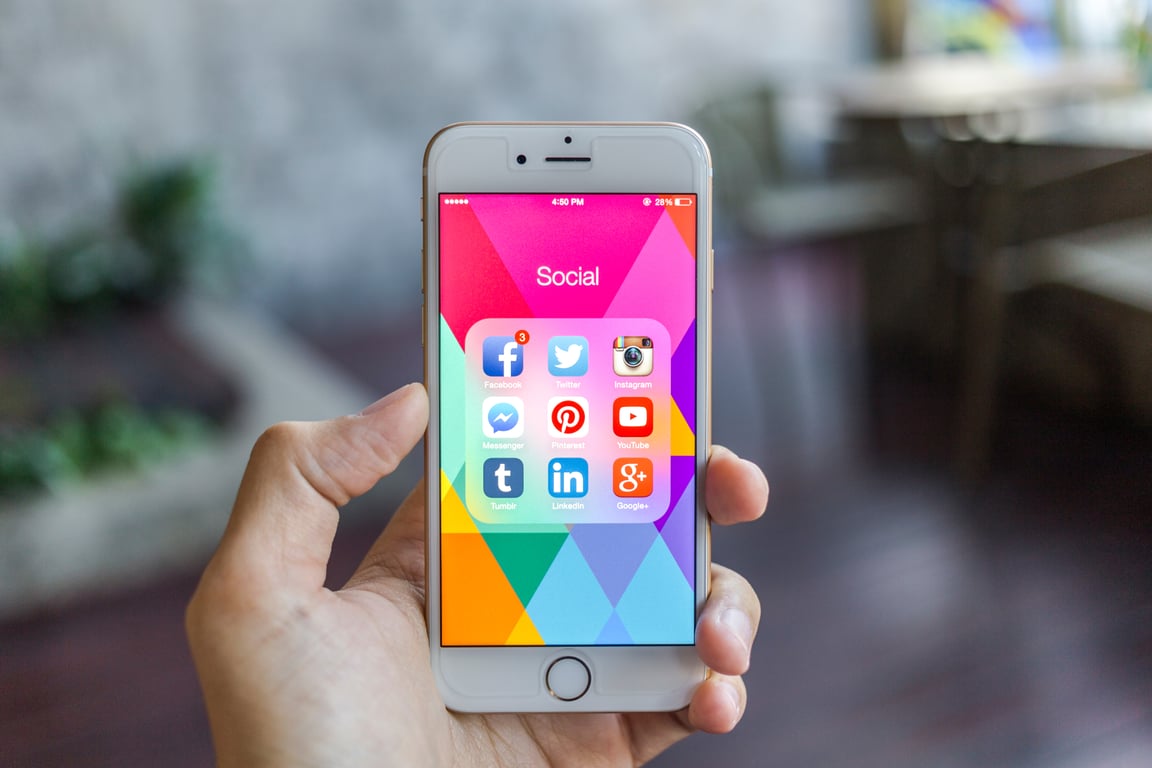 Cropped image of hand holding smartphone displaying grid of popular social media app icons